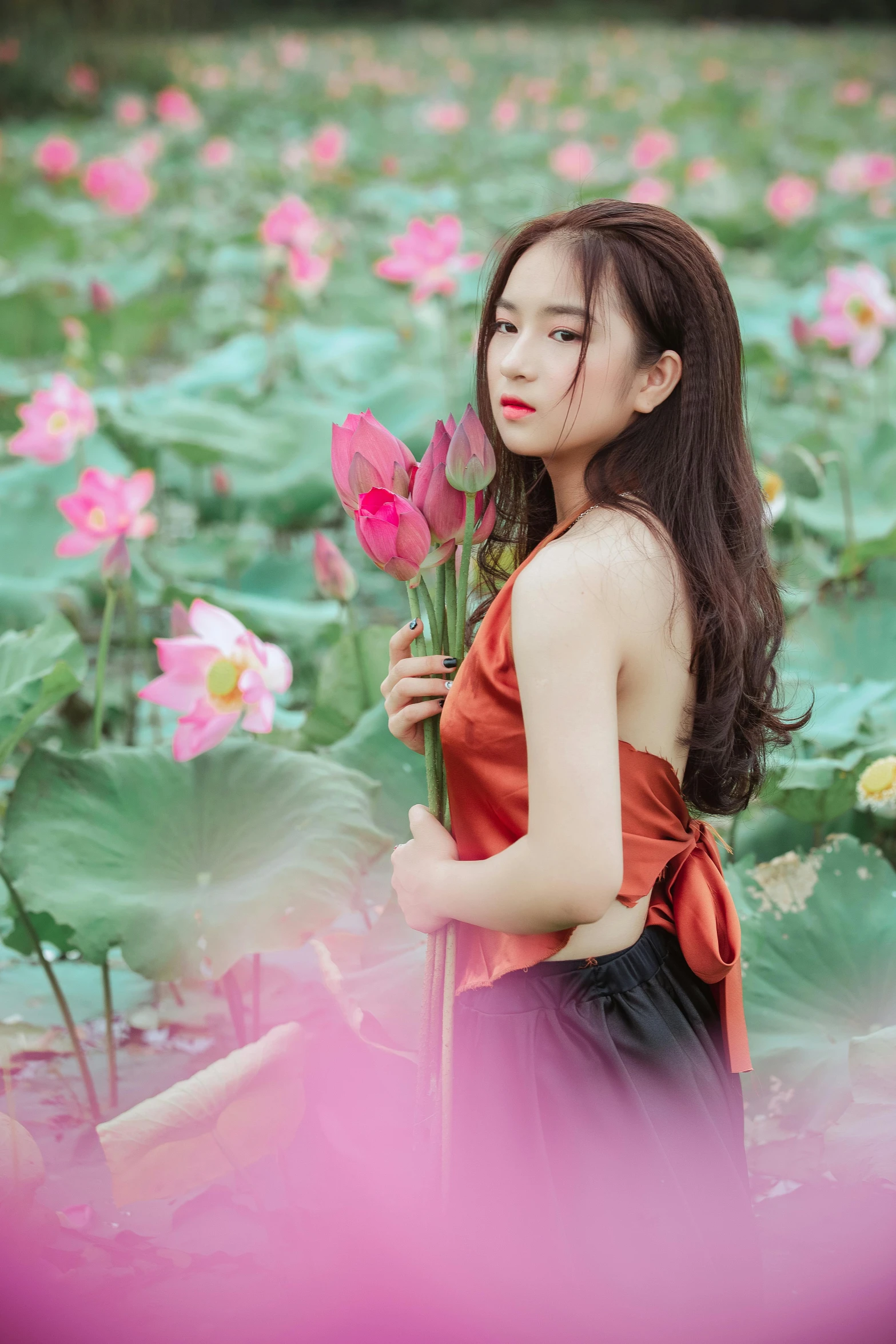 a woman standing in a field of pink flowers, inspired by Shao Mi, renaissance, standing gracefully upon a lotus, 5 0 0 px models, 1 8 yo, red