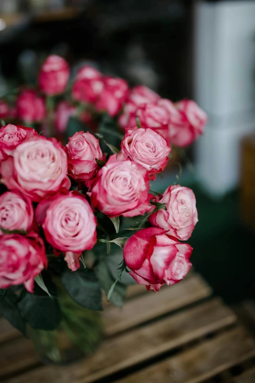 a vase filled with pink roses sitting on top of a wooden table, by Elsie Few, unsplash, flower shop scene, low detail, fully covered, small red roses