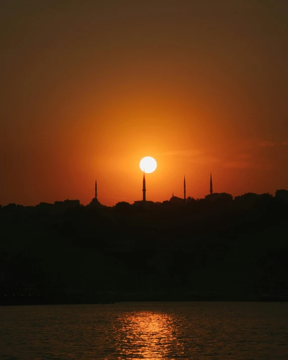 the sun is setting over a body of water, by Attila Meszlenyi, pexels contest winner, hurufiyya, minarets, sunburn, high quality photo, heat shimmering