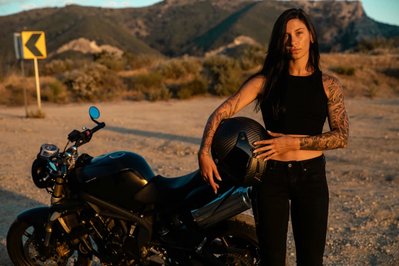 a woman standing next to a motorcycle in the desert, a portrait, by Lee Loughridge, pexels contest winner, symbolism, wearing a cropped black tank top, with tattoos, ayne haag, portrait of tifa lockhart