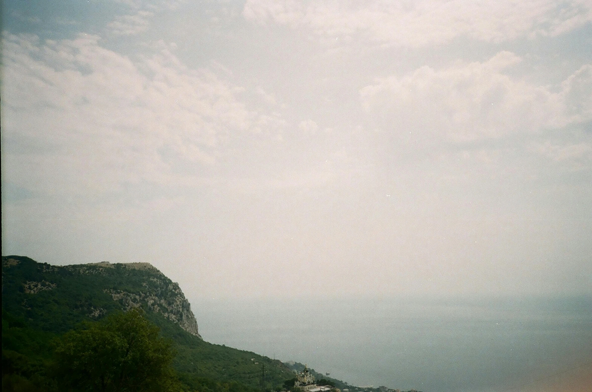 a man flying a kite on top of a lush green hillside, a picture, by Pablo Rey, unsplash, romanticism, capri coast, expired film, distant clouds, hazy