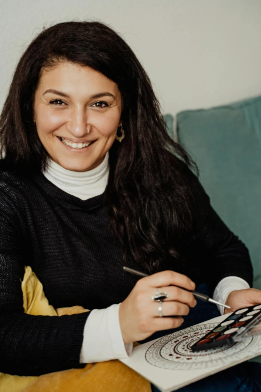 a woman sitting on a couch holding a pen and drawing, inspired by Ion Andreescu, pexels contest winner, smiling at the camera, shohreh aghdashloo, studio ghilbi, profile image