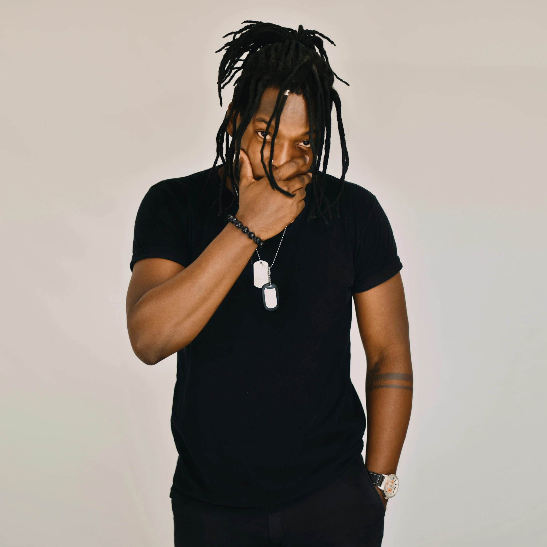 a man with dreadlocks standing in front of a white wall, trending on pexels, wearing a black shirt, ( ( dark skin ) ), band, thinker pose