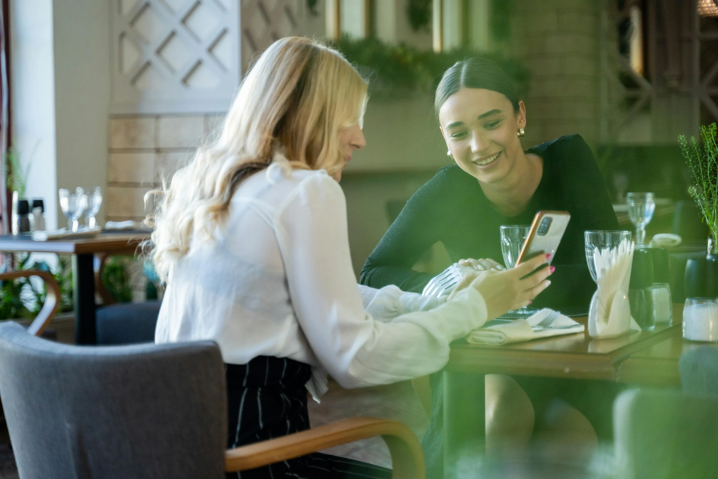 two women sitting at a table looking at a cell phone, pexels contest winner, happening, elegant look, avatar image, seasonal, casually dressed