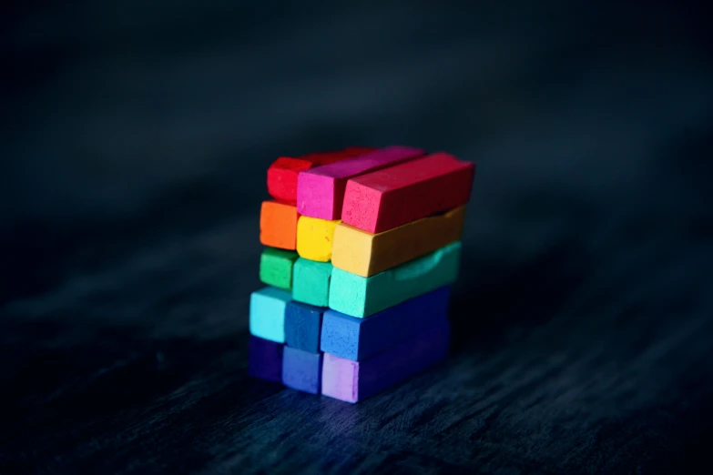 a stack of colorful blocks sitting on top of a wooden table, by Emma Andijewska, unsplash, with a black background, indigo rainbow, cube, solid color