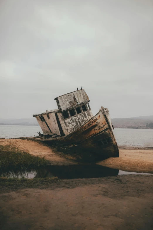 a boat sitting on top of a beach next to a body of water, unsplash contest winner, building crumbling, faded worn, stern, tall