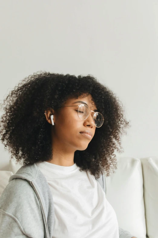 a woman sitting on a couch using a laptop, trending on pexels, renaissance, earbuds, portrait of mournful, mixed race woman, wearing small round glasses