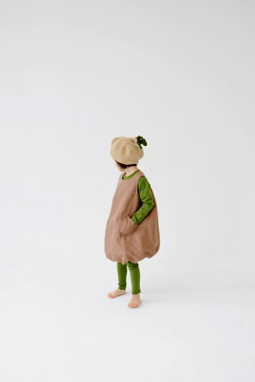 a figurine of a person standing on a white surface, green and brown clothes, tiny girl looking on, full product shot, ignant