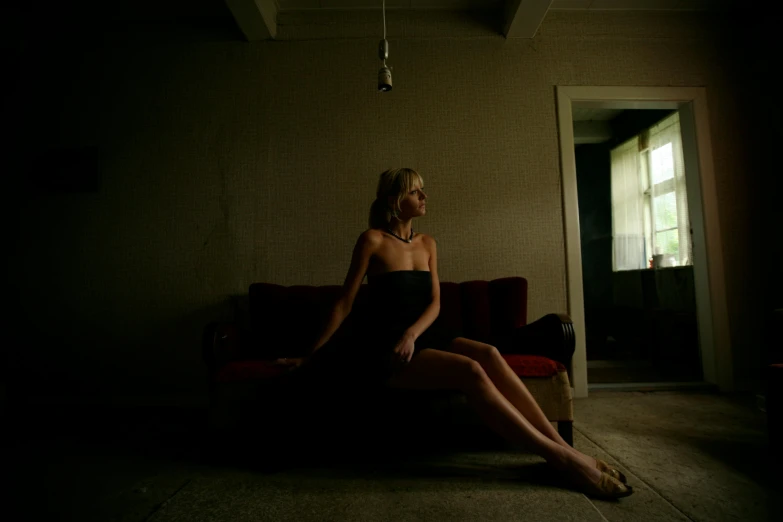 a woman sitting on a couch in a dark room, an album cover, inspired by Nan Goldin, unsplash contest winner, blonde, dark dress, greg crewdson, movie still 8 k