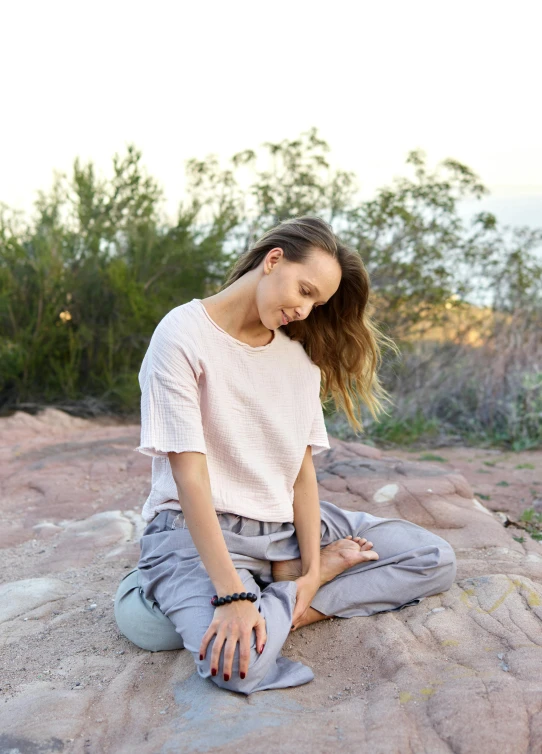 a woman sitting on top of a large rock, wearing a linen shirt, pink and grey muted colors, wearing a tee shirt and combats, in australia