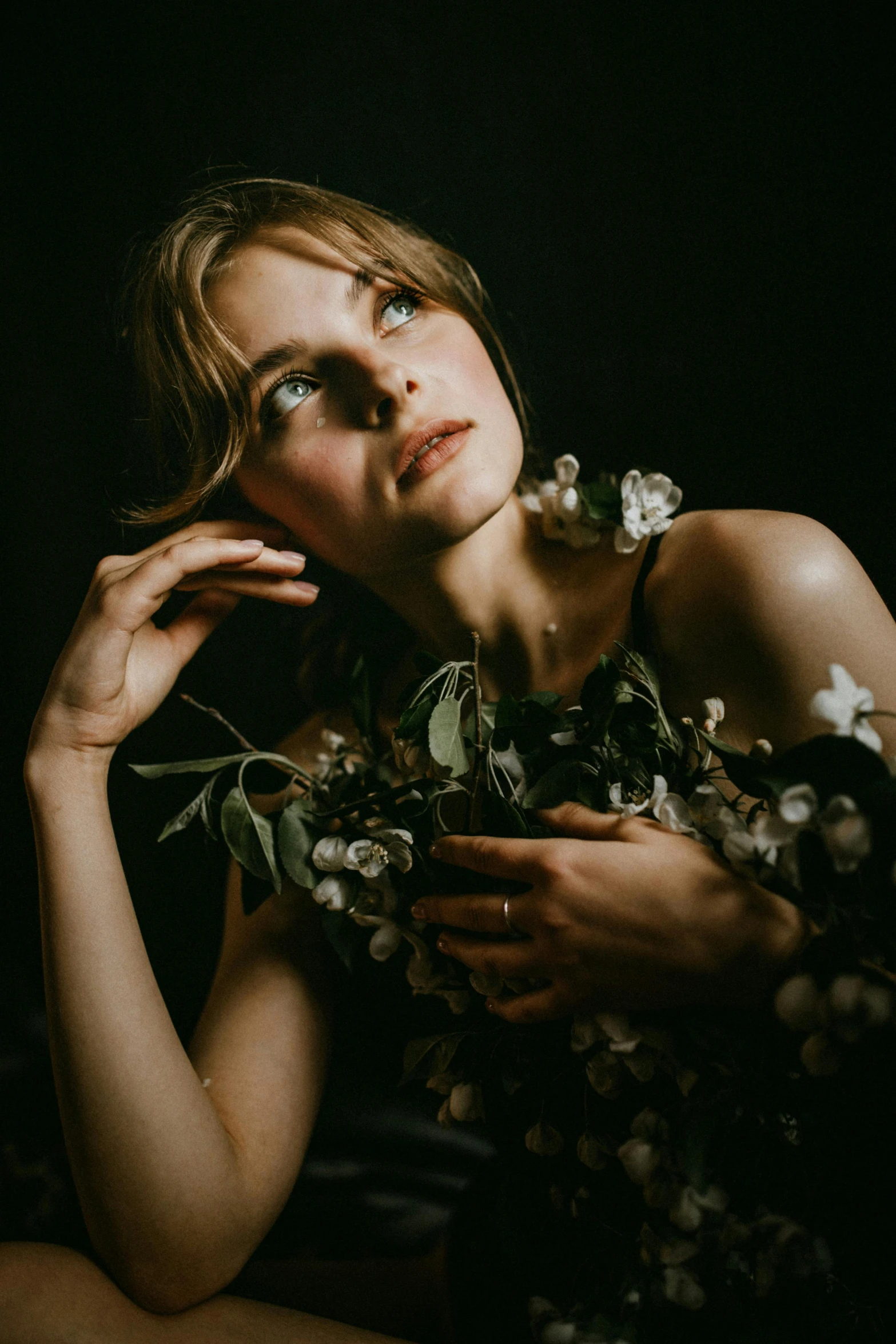 a woman in a black dress holding a bouquet of flowers, a portrait, inspired by Elsa Bleda, unsplash contest winner, side portrait of imogen poots, branches sprouting from her head, dark. studio lighting, taken in the early 2020s