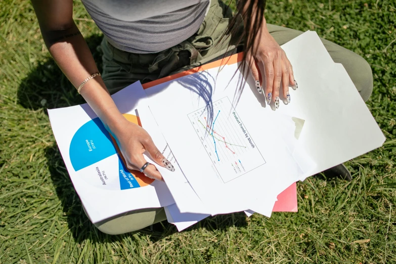 a woman sitting on the ground with a bunch of papers, unsplash, academic art, informative graphs and diagrams, sydney park, barometric projection, closeup photograph