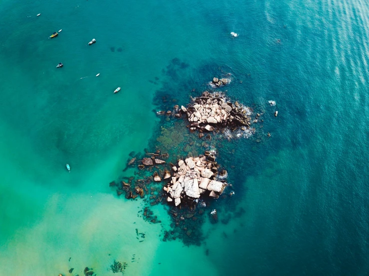 a group of people riding surfboards on top of a body of water, a tilt shift photo, pexels contest winner, minimalism, reefs, glowing hue of teal, with water and boats, helicopter view