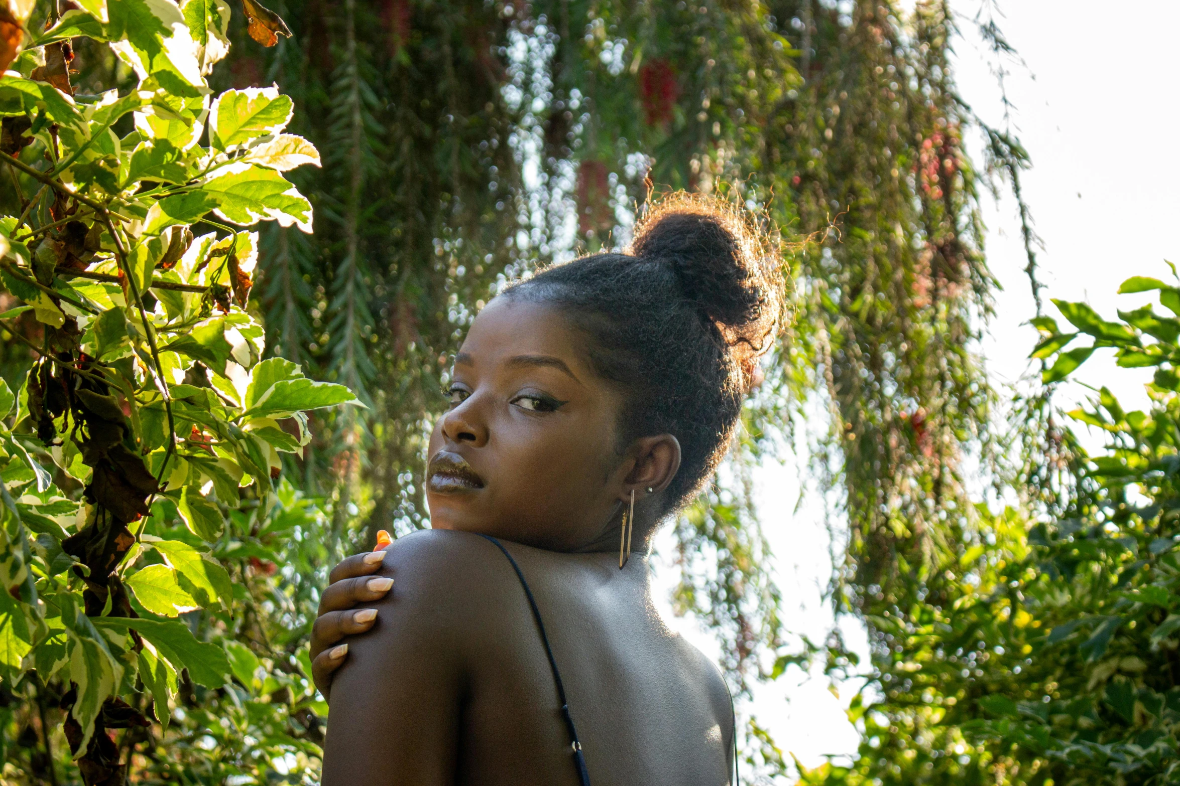 a woman in a bikini posing for a picture, by Lily Delissa Joseph, unsplash, afrofuturism, under the soft shadow of a tree, lush greens, black teenage girl, showing her shoulder from back