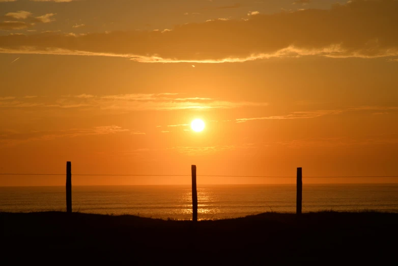 a view of the sun setting over the ocean, a picture, by Jan Tengnagel, pexels contest winner, romanticism, fence line, cornwall, golden hues, late summer evening