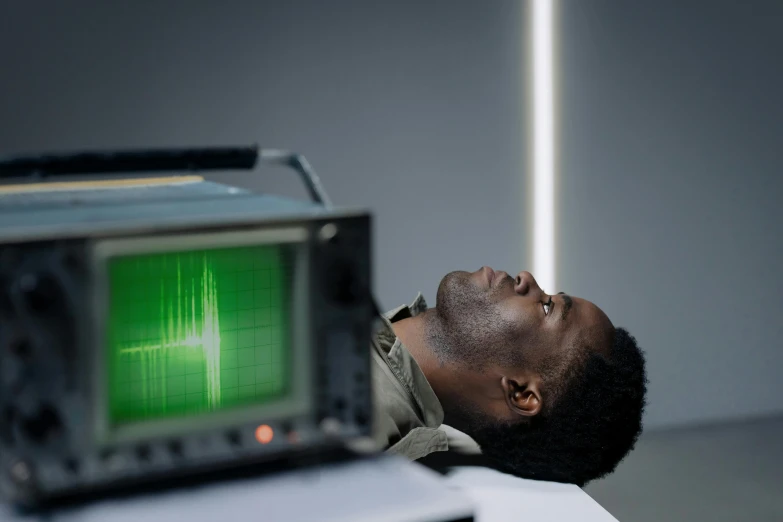 a man laying on top of a desk next to a television, unsplash, holography, oscilloscope, idris elba as james bond, stood in a lab, doppler effect
