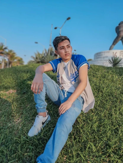 a man sitting in the grass next to a statue, by Ismail Acar, instagram, realism, teen boy, casual pose, from egypt, outfit photo