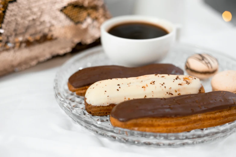 a glass plate topped with pastries next to a cup of coffee, by Emma Andijewska, pexels contest winner, hurufiyya, chocolate sauce, pointè pose, shiny and metallic, on a pale background