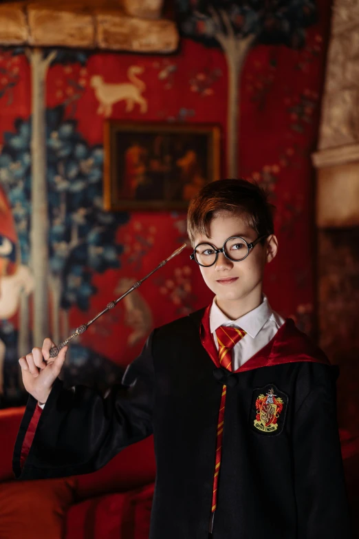 a boy in a harry potter costume holding a wand, a portrait, pexels contest winner, happening, hogwarts gryffindor common room, spectacles, embroidered robes, avatar image