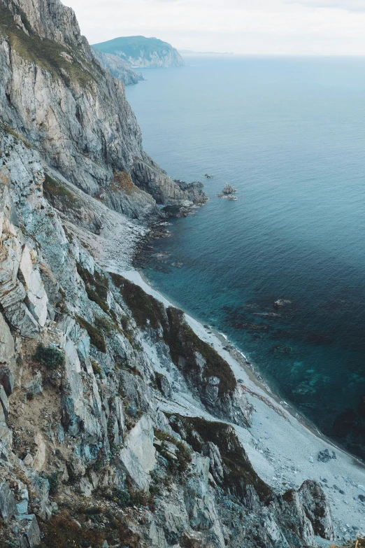 a man standing on top of a cliff next to the ocean, inspired by Elsa Bleda, unsplash contest winner, hyperrealism, “ aerial view of a mountain, steep cliffs, calmly conversing 8k, teal color graded