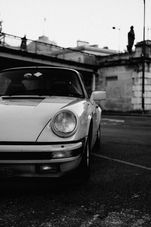 a white sports car parked on the side of the road, a black and white photo, inspired by Harry Haenigsen, unsplash, 2 5 6 x 2 5 6, paris 1982, porsche 911, dirty streets