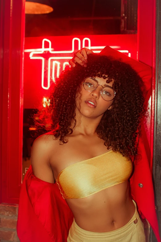 a woman posing for a picture in front of a neon sign, inspired by Nan Goldin, trending on pexels, renaissance, gold transparent bikini, mixed race woman, wearing red tainted glasses, yellow clothes