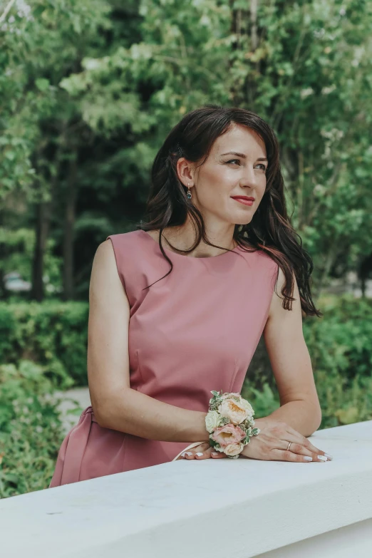 a woman in a pink dress sitting on a ledge, a colorized photo, inspired by Adrienn Henczné Deák, pexels contest winner, wearing elegant jewellery, wearing business casual dress, sitting in the rose garden, sitting on a mocha-colored table