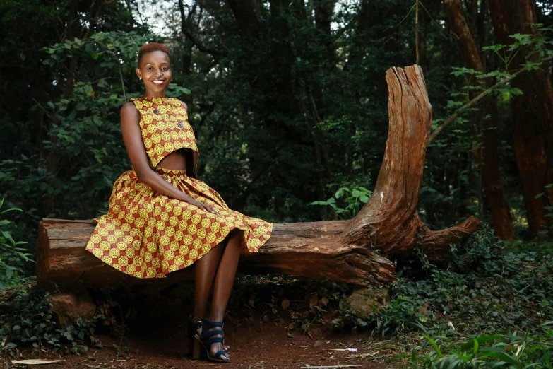 a woman sitting on a log in the woods, inspired by Afewerk Tekle, pexels contest winner, hurufiyya, wearing an african dress, while smiling for a photograph, wide skirts, unmistakably kenyan