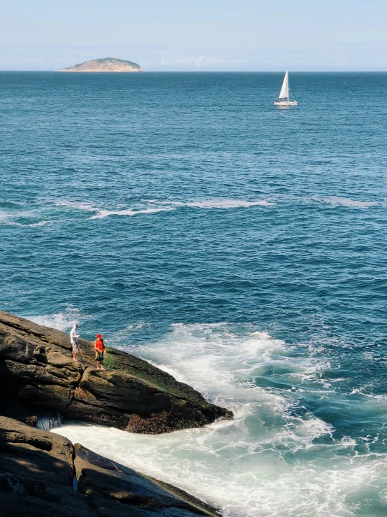 a couple of people standing on top of a rock next to the ocean, sailboats in the water, roaring ocean in front, slide show, new hampshire