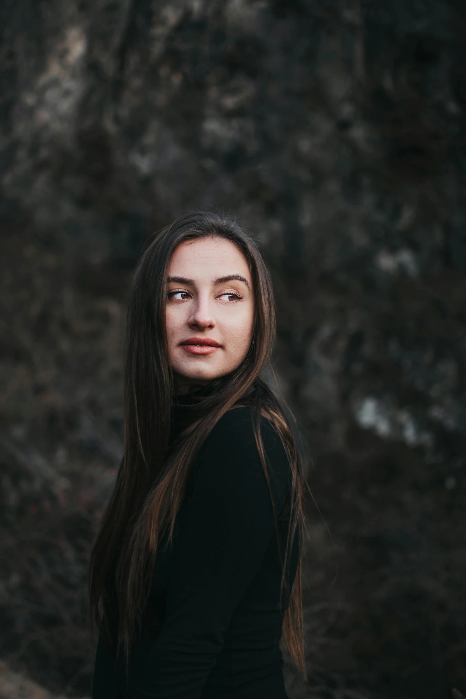 a woman standing in front of a rock wall, by irakli nadar, brown long and straight hair, wearing a black sweater, portrait featured on unsplash, headshot profile picture