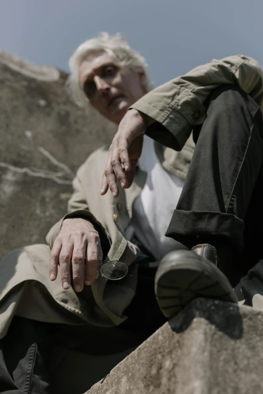 a man sitting on top of a large rock, inspired by Joseph Beuys, unsplash, photorealism, gray haired, [ cinematic, key still, long fingers