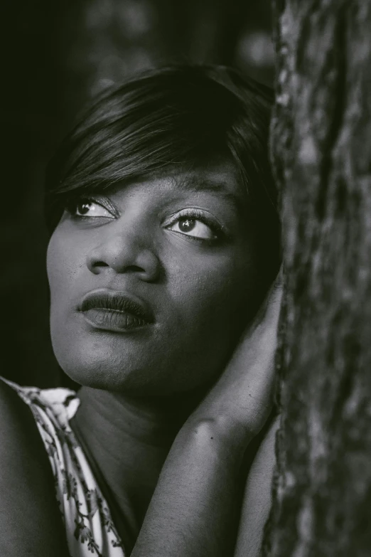 a black and white photo of a woman leaning against a tree, inspired by Thomas Blackshear, rihanna, on a dark background, determined expression, close - up portrait