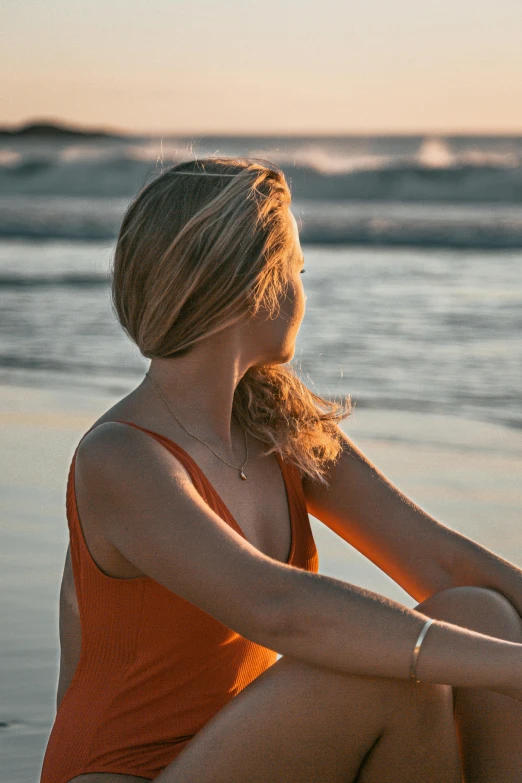 a woman sitting on a beach next to the ocean, orange hue, sunbathed skin, profile pic, meditative