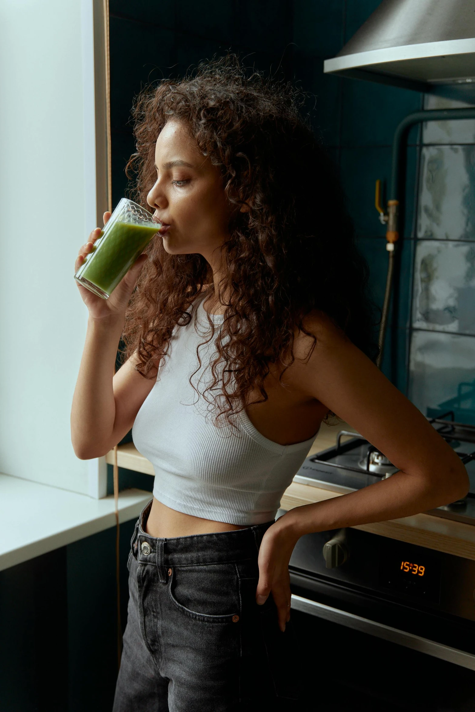 a woman drinking a green smoothie in a kitchen, trending on pexels, renaissance, portrait sophie mudd, curls, 6 pack, profile pose