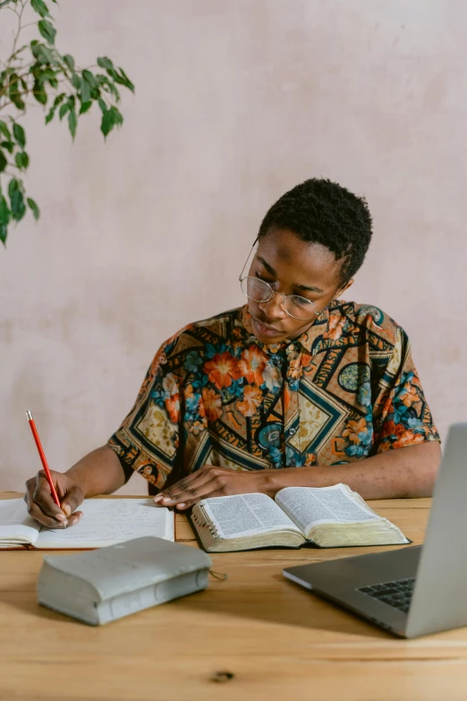 a man sitting at a table with a laptop and a notebook, trending on pexels, academic art, patterned clothing, african woman, christian, young commoner