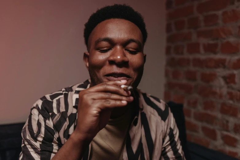 a man sitting in front of a brick wall, childish gambino, praying with tobacco, portrait featured on unsplash, sitting in a lounge