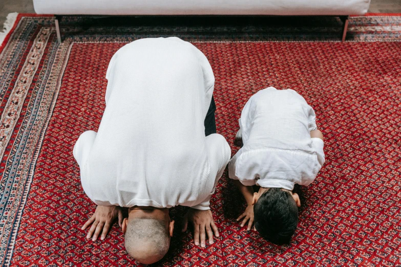 a couple of men standing on top of a red rug, pexels contest winner, hurufiyya, bent over posture, muslim, with a kid, head straight down