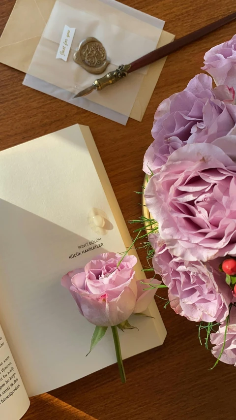 a bouquet of flowers sitting on top of a table next to an open book, greeting card, taken on iphone 1 3 pro, low quality photo, pink bees