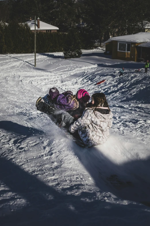 a person riding a snowboard down a snow covered slope, kids playing, outside on the ground, in the winter, piled around