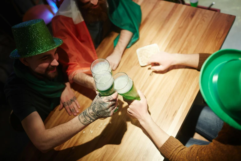 a group of people sitting around a wooden table, green flags, holding a drink, abcdefghijklmnopqrstuvwxyz, irish