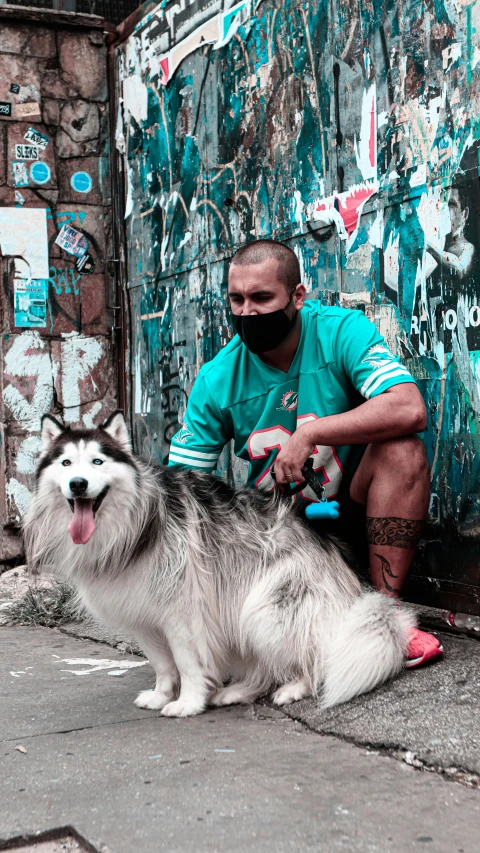 a man sitting next to a dog on a sidewalk, a colorized photo, by Basuki Abdullah, pexels contest winner, graffiti, green facemask, husky, portrait of rugged zeus, white and teal garment