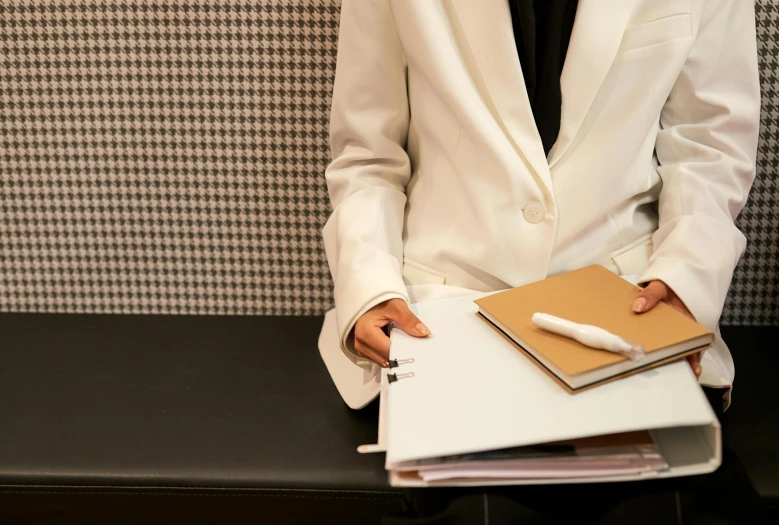 a man in a white suit holding a notebook and pen, an album cover, by Nicolette Macnamara, trending on unsplash, private press, female in office dress, white hijab, sitting in a waiting room, papers on table