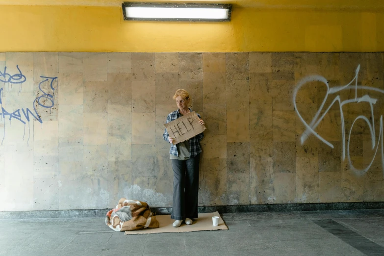 a person standing in front of a wall with graffiti on it, a photo, homeless, holding a gold bag, an elderly, filmstill