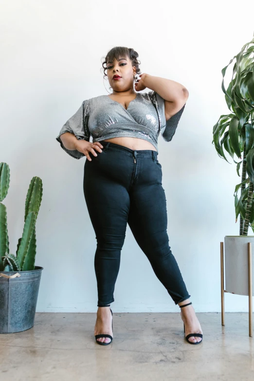 a woman standing in front of a cactus plant, trending on pexels, black extremely tight jeans, bbw, in gunmetal grey, complex outfit