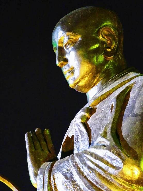 a close up of a statue of a person, at night time, buddhist architecture, yellow lighting from right, in a silver silk robe