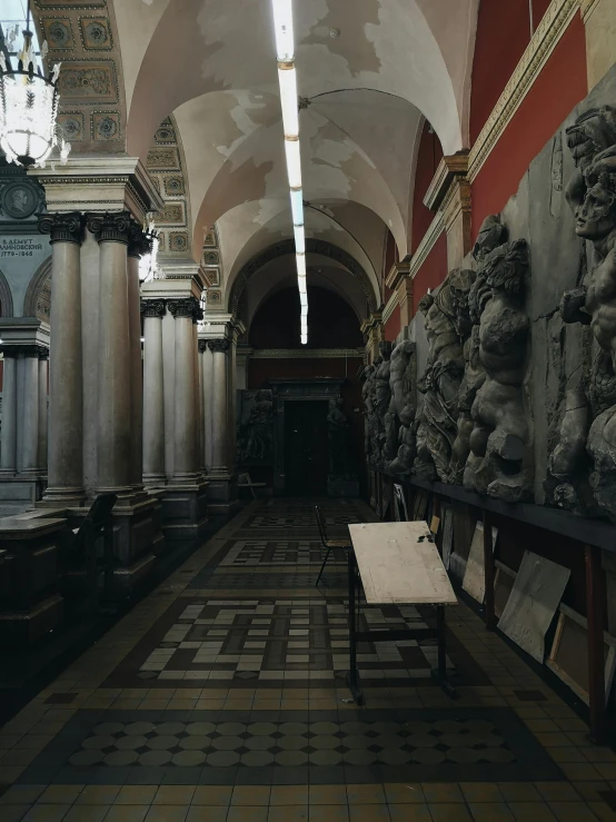 a long hallway in a building with sculptures on the walls, inspired by Károly Markó the Elder, academic art, low quality photo, inside a tomb, captured in low light, looking the camera