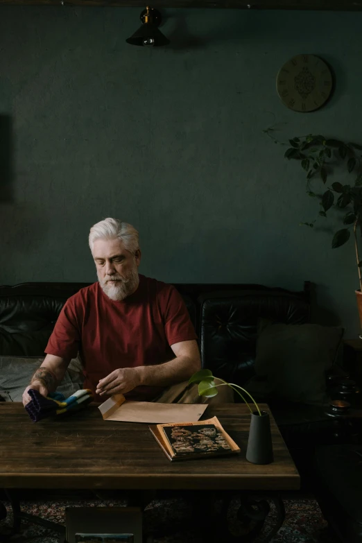 a man sitting at a table using a cell phone, a character portrait, pexels contest winner, photorealism, short white beard, vhs colour photography, in a living room, aboriginal australian hipster