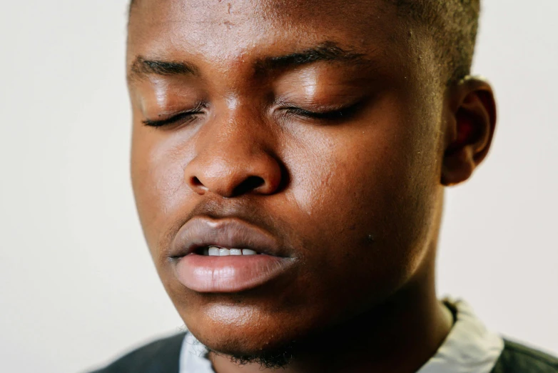 a close up of a man with his eyes closed, by Daniel Lieske, trending on unsplash, emmanuel shiru, around 1 9 years old, plain background, mongezi ncaphayi