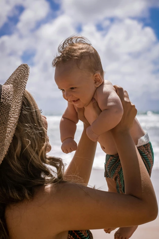 a woman holding a baby on the beach, by Will Ellis, square, mango, super high resolution, bedhead