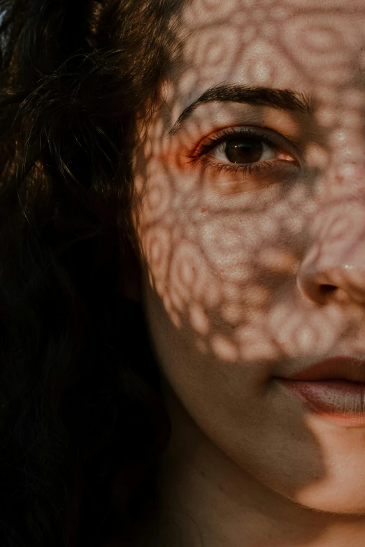 a close up of a person with long hair, her face is in shadow, portrait featured on unsplash, intricate patterns on face, soft sun lights